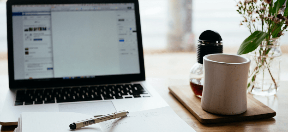 a desk with a laptop, coffee cup and notebook