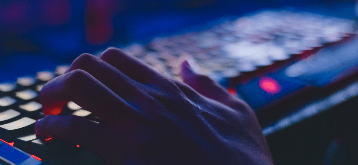 A person typing on a keyboard that is lit up against a dark background