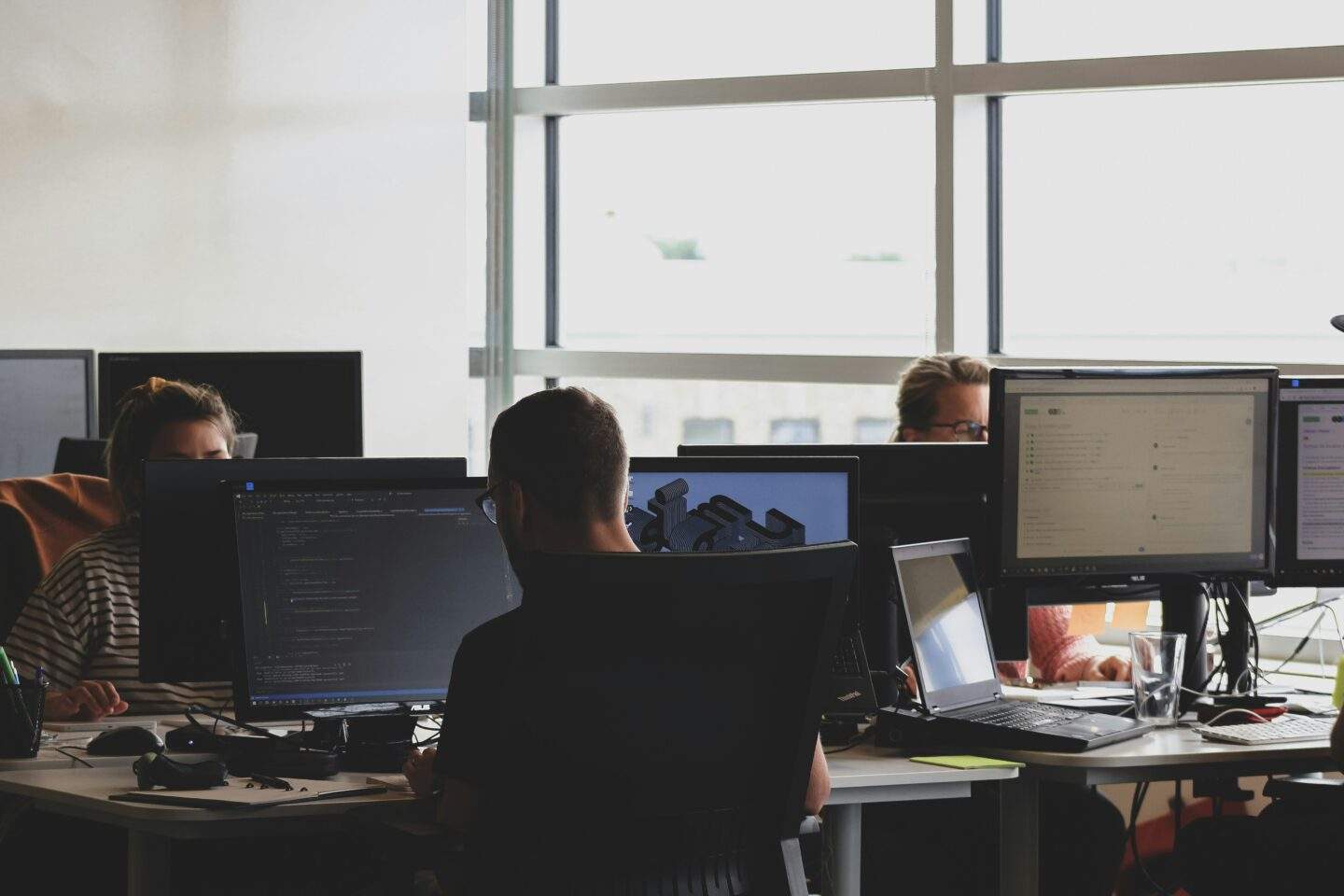 Cybersecurity team members working at computer monitors in a modern office, focusing on code and threat analysis.