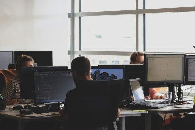 Cybersecurity team members working at computer monitors in a modern office, focusing on code and threat analysis.