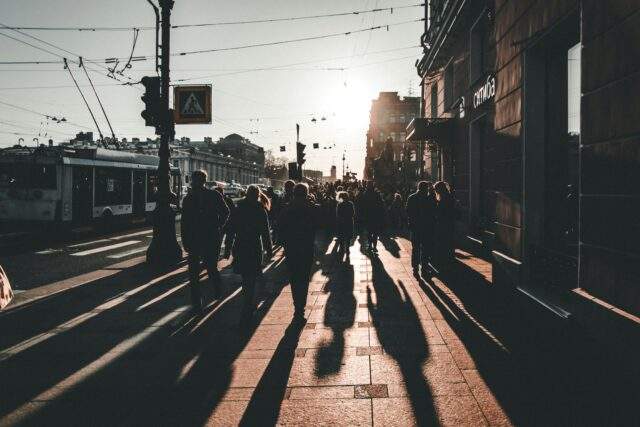 Abstract image of people walking with long shadows on a city street, symbolising human presence guiding automation in offensive security.