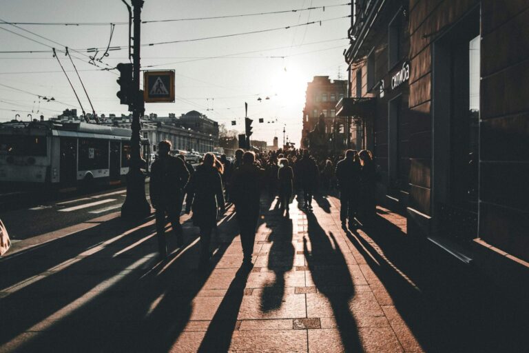 Abstract image of people walking with long shadows on a city street, symbolising human presence guiding automation in offensive security.