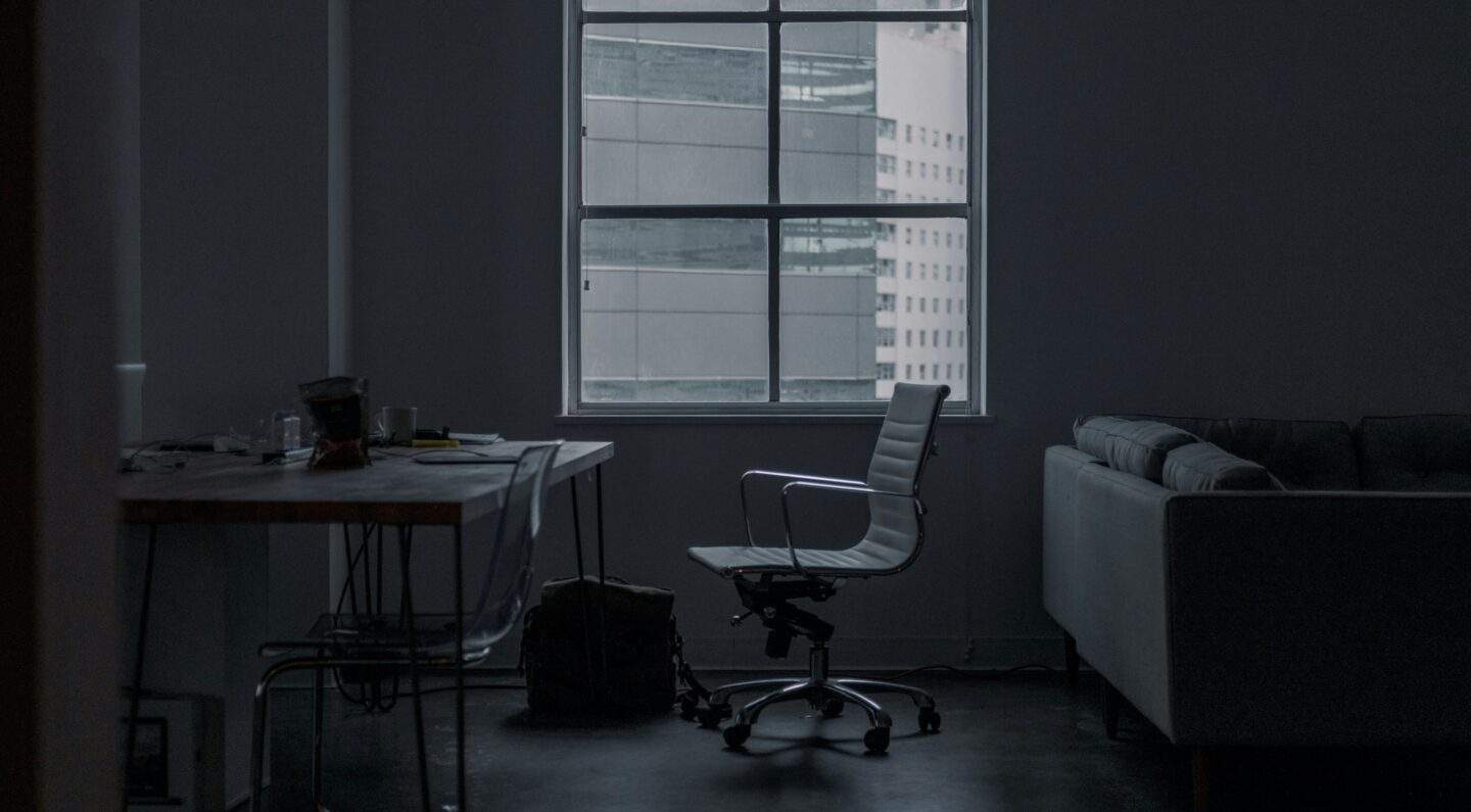 Dark office with an empty chair by a window representing constant cyber attack and unseen threats