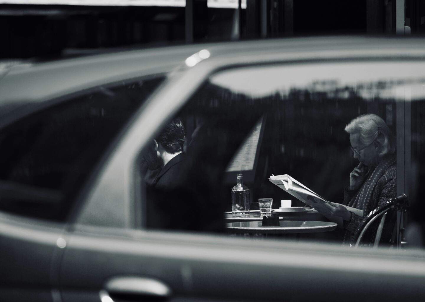Black and white surveillance perspective view of people at a table through a car window, symbolizing covert observation and offensive security reconnaissance