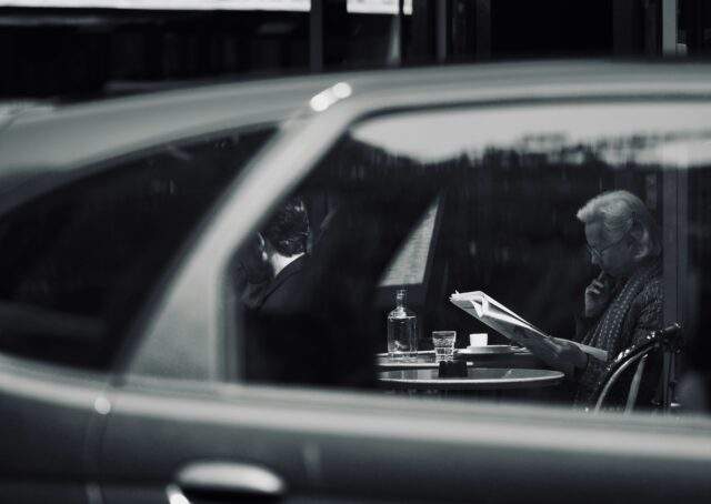 Black and white surveillance perspective view of people at a table through a car window, symbolizing covert observation and offensive security reconnaissance