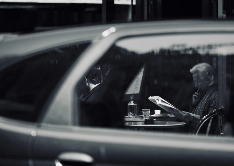 Black and white surveillance perspective view of people at a table through a car window, symbolizing covert observation and offensive security reconnaissance