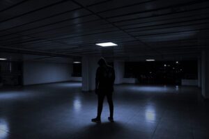 Silhouette of person in dark environment representing insider threat in agentic IDE security with code and terminal windows in background