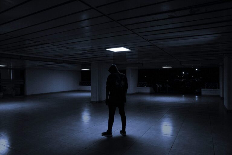 Silhouette of person in dark environment representing insider threat in agentic IDE security with code and terminal windows in background