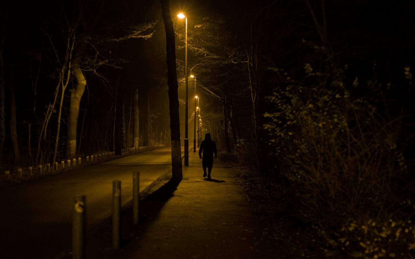 A lone figure walks away down a dark, empty street at night, unseen and undetected.