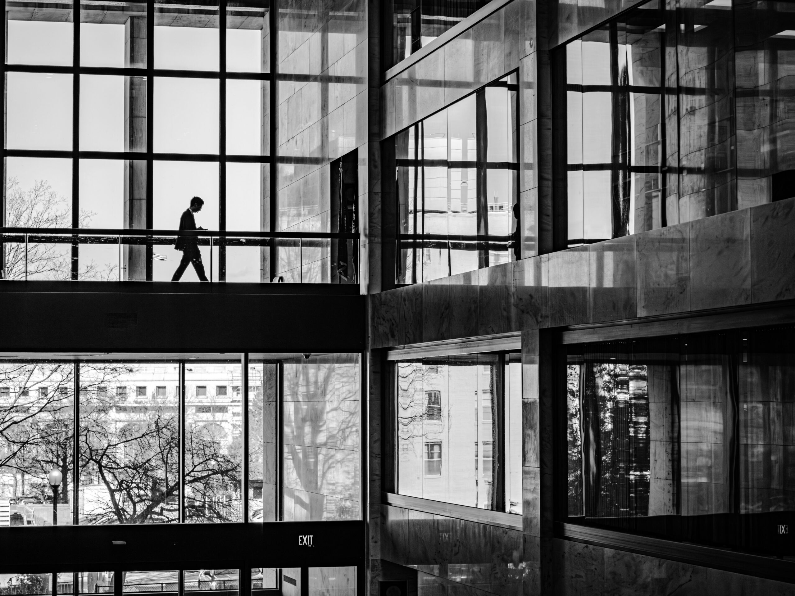 Black-and-white photo of a silhouetted person walking through a glass-and-marble office atrium, unaware of what's exposed just out of sight.