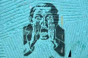 Alt text "Stencil street art of a man in a suit, one hand pressed to his face, mouth open mid-scream, on a teal wall — symbolizing loss of control and panic in the face of a security breach.