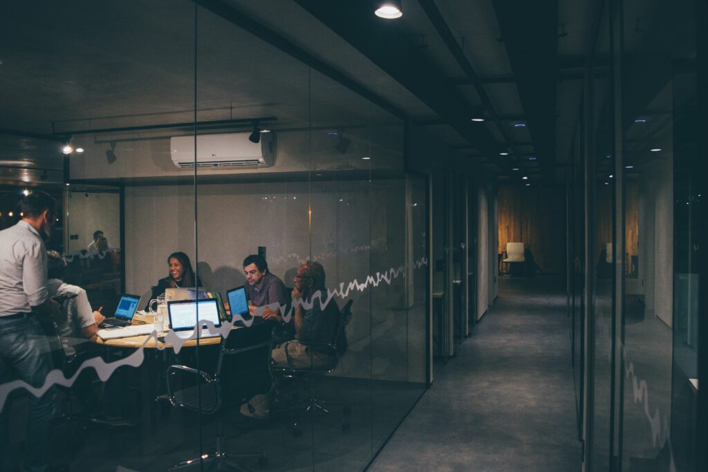 A brightly lit glass office meeting room beside a long, empty, dimly lit corridor, evoking the unguarded physical access gap that physical security testing exists to catch.