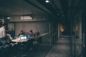 A brightly lit glass office meeting room beside a long, empty, dimly lit corridor, evoking the unguarded physical access gap that physical security testing exists to catch.