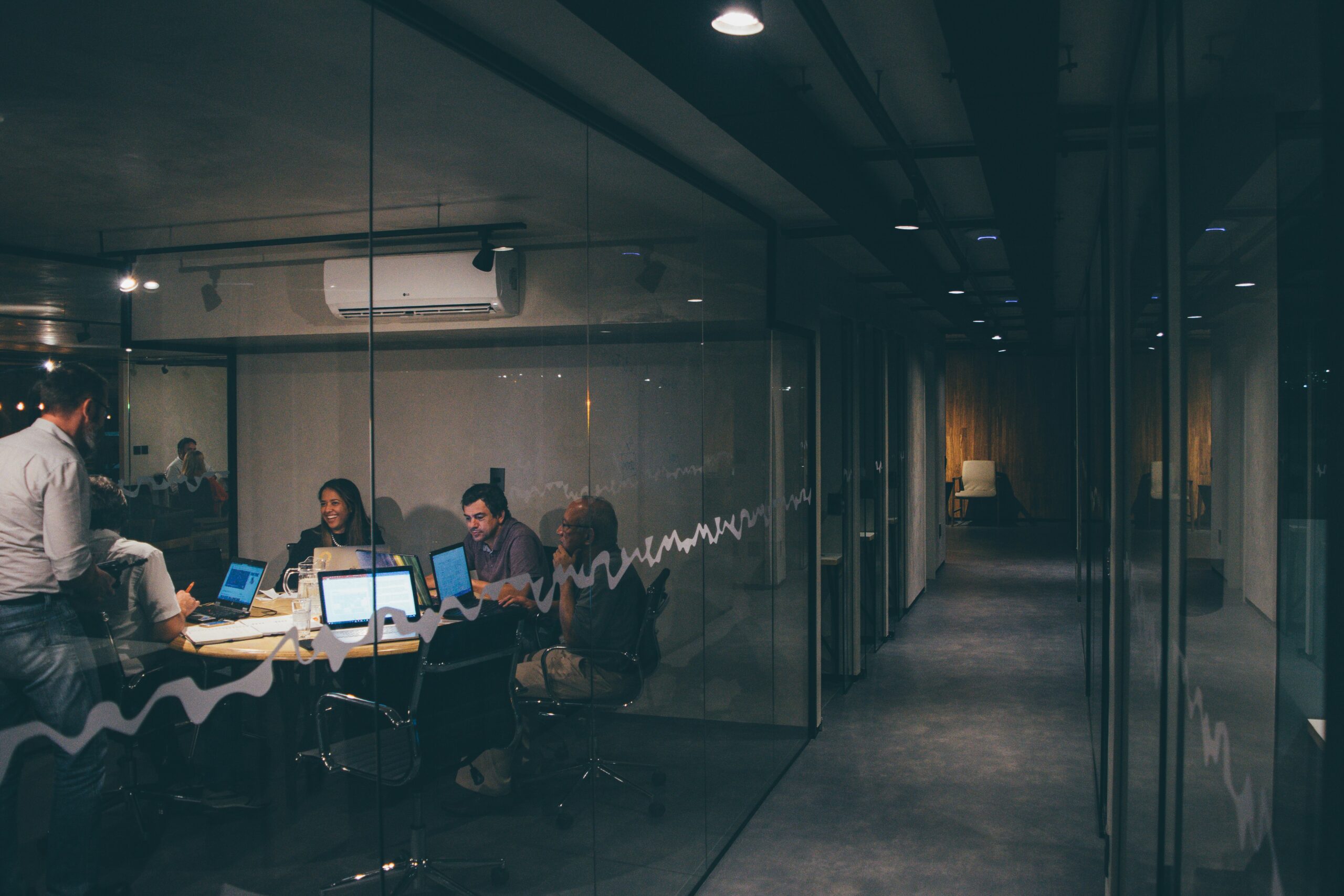 A brightly lit glass office meeting room beside a long, empty, dimly lit corridor, evoking the unguarded physical access gap that physical security testing exists to catch.