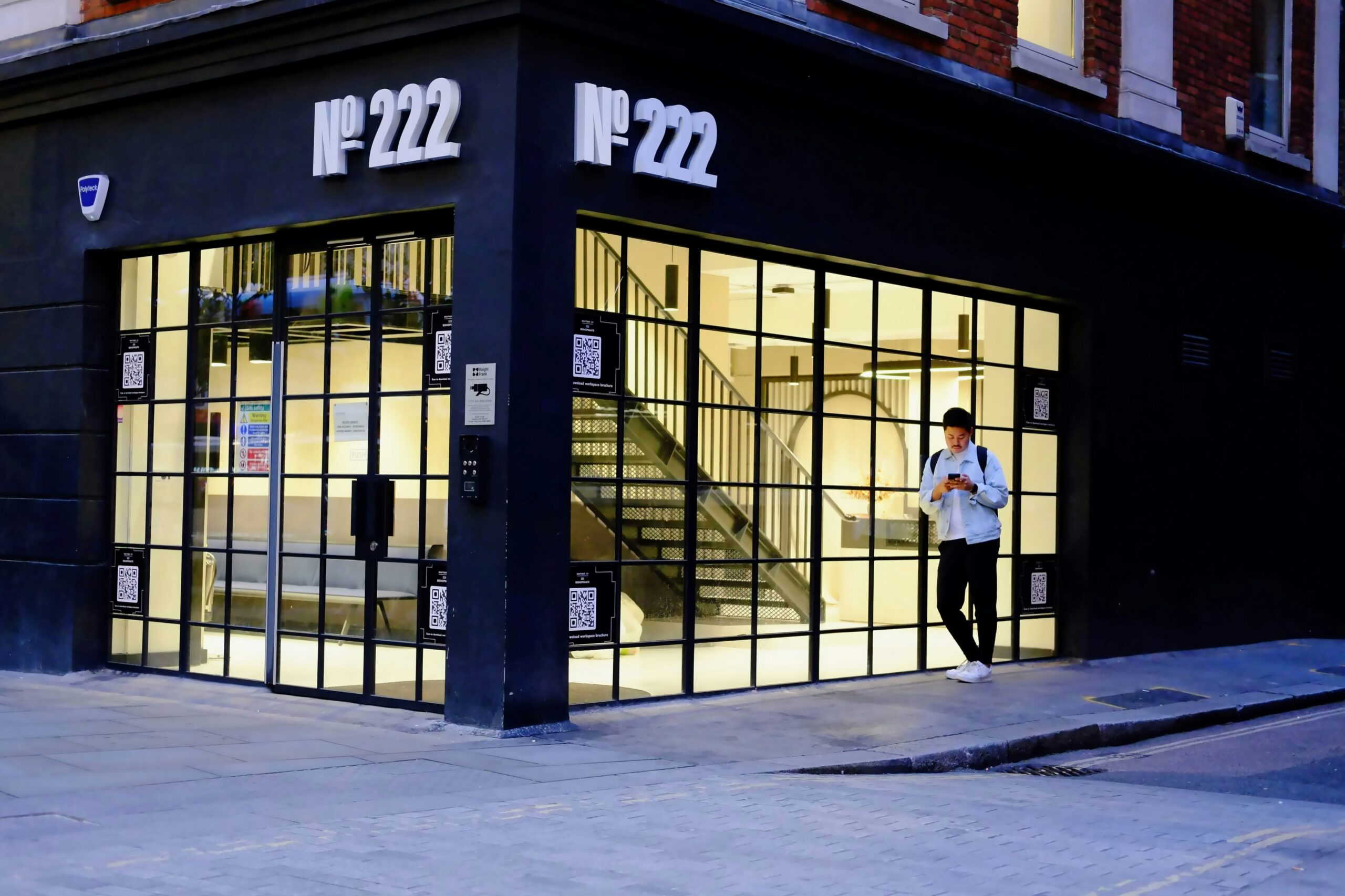 A man checks his phone outside a lit office entrance at dusk, evoking the moment of trust a social engineering attack exploits before anyone steps through the door.