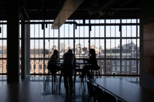 Silhouetted colleagues in quiet discussion against a city skyline, evoking the trusted, routine approval a business email compromise exploited.
