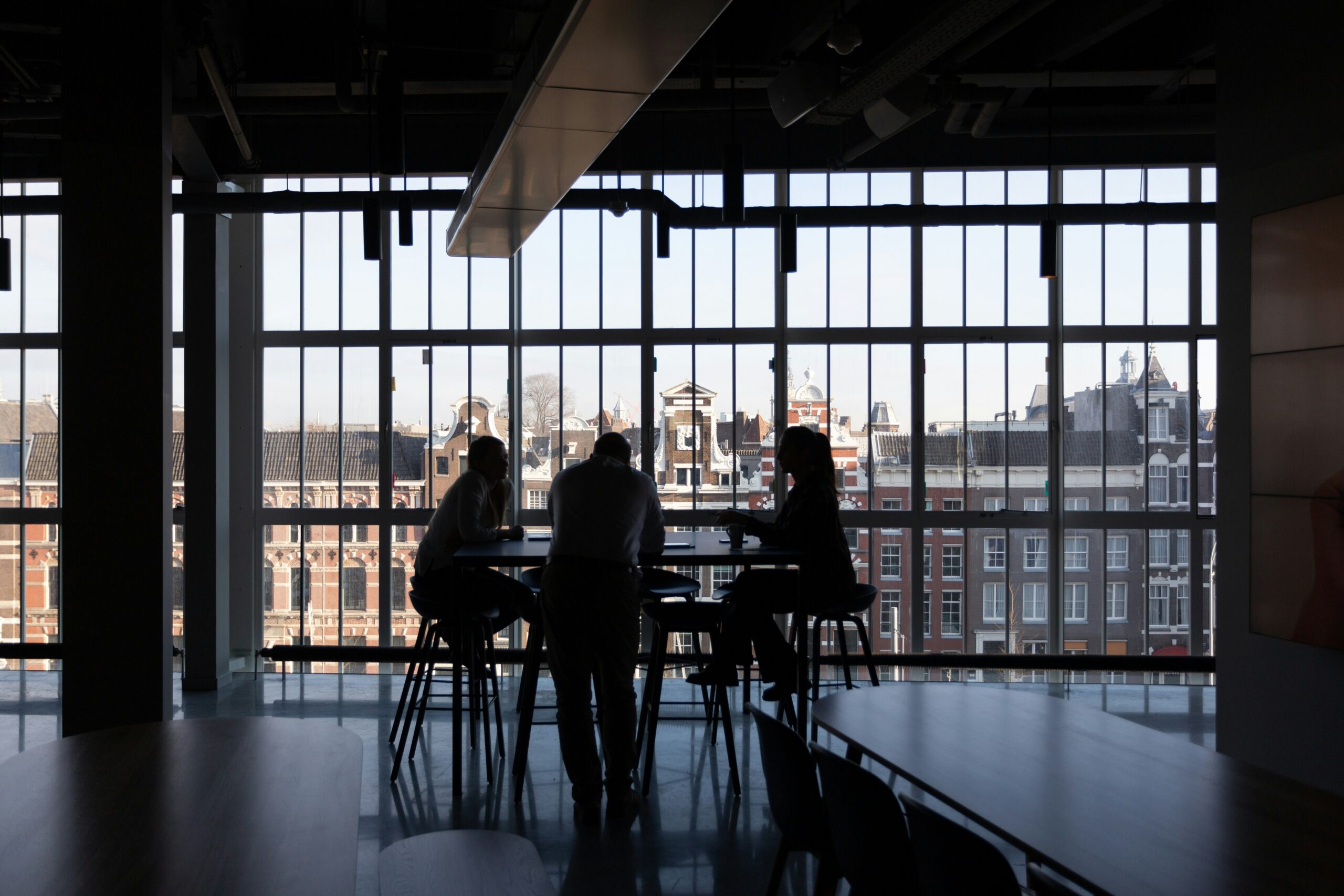 Silhouetted colleagues in quiet discussion against a city skyline, evoking the trusted, routine approval a business email compromise exploited.