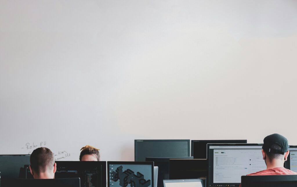 Employees working at their monitors, heads down, unaware their help desk is fielding a vishing attack disguised as a routine password reset.