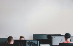 Employees working at their monitors, heads down, unaware their help desk is fielding a vishing attack disguised as a routine password reset.