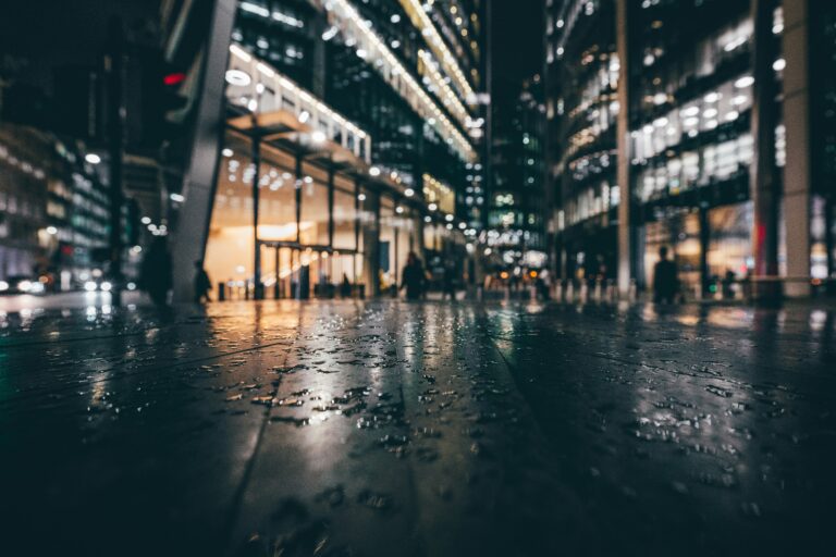 Rain-soaked pavement at night in front of brightly lit glass office buildings, a picture of cyber hygiene that looks secure on the surface