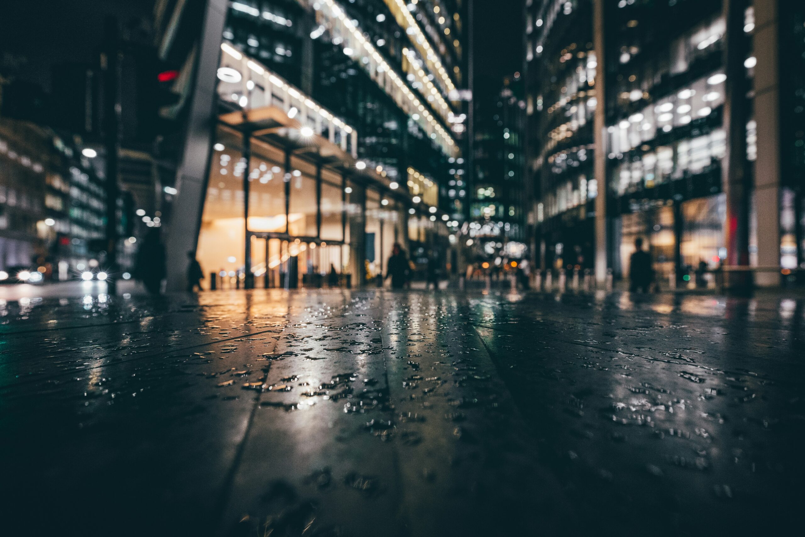 Rain-soaked pavement at night in front of brightly lit glass office buildings, a picture of cyber hygiene that looks secure on the surface