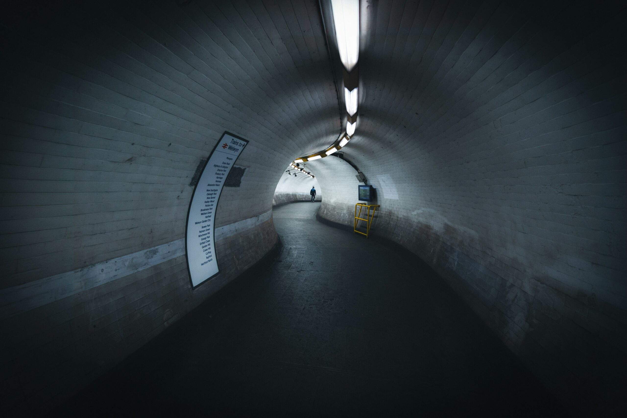 Dim curved tunnel with a lone figure walking ahead, representing an agentic testing investigation
