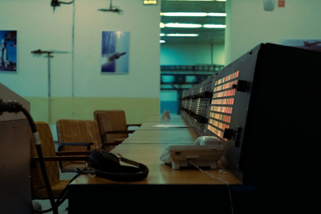 Empty operations control room with a long console of lit indicator panels, a headset and desk phone, the kind of environment where defenders would need to spot a real attack.